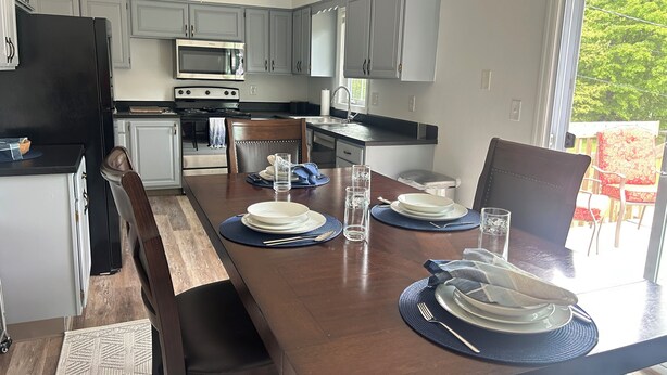 A modern kitchen with grey cabinets, a black refrigerator, a microwave, and a stove. There is a dining table set with plates, glasses, and cutlery. - Sunnyside Suite in peaceful Cambridge Springs (Cambridge Springs)
