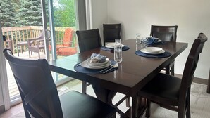 A dining area with a table set for four, chairs, and a view of a wooden deck and greenery outside. - Sunnyside Suite in peaceful Cambridge Springs (Cambridge Springs)