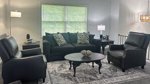 A living room with a dark-colored sofa, two armchairs, a coffee table, and a patterned rug. - Sunnyside Suite in peaceful Cambridge Springs (Cambridge Springs)