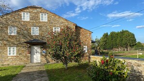 Un bâtiment en pierre avec un petit porche et un arbre aux fleurs rouges devant.