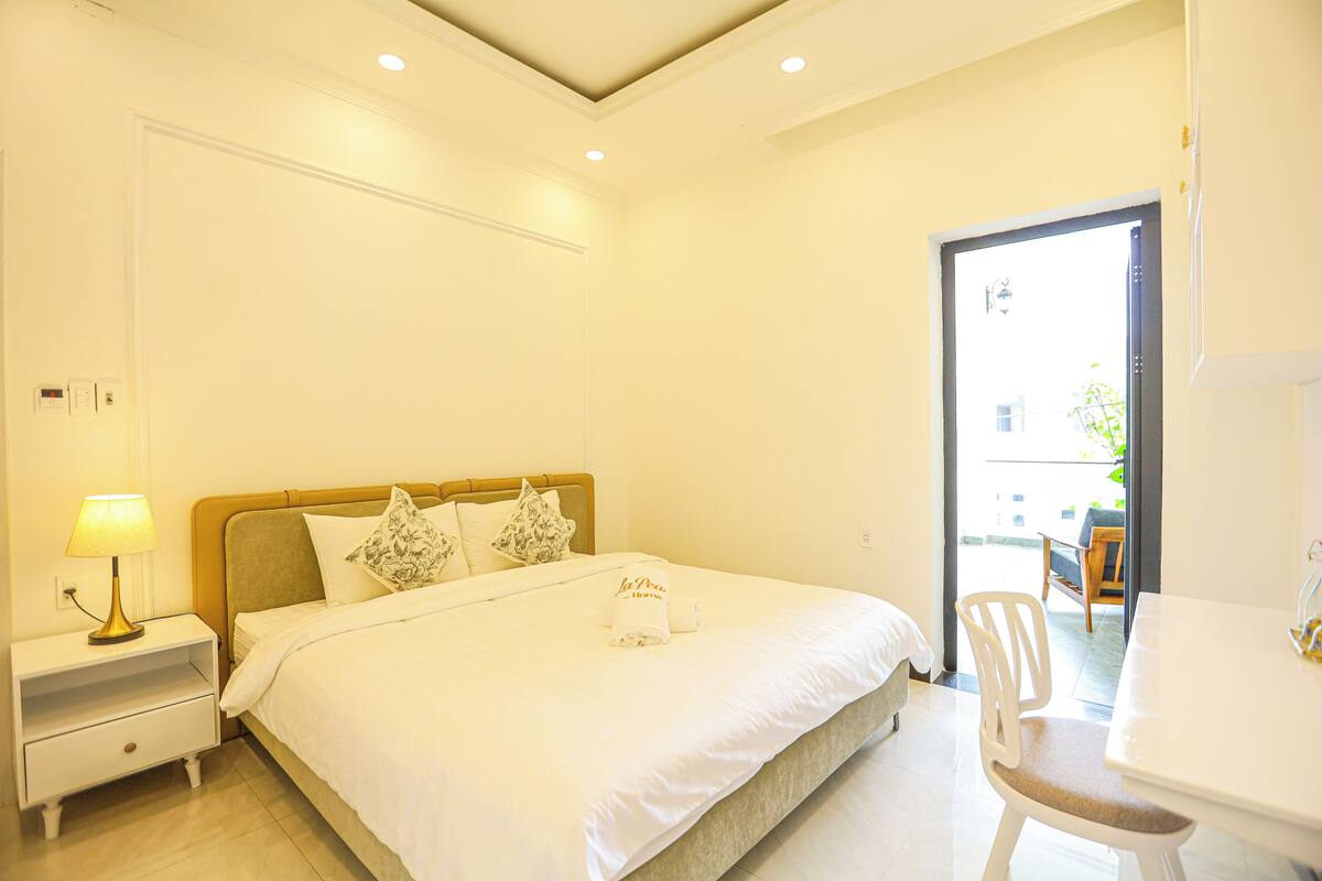 A hotel room with a bed, bedside table, lamp, and a view of the outside.