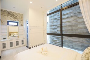 A hotel room with a large bed, a vanity with a mirror, and a view of a stone wall through a window. - La Peace Home (Hue)