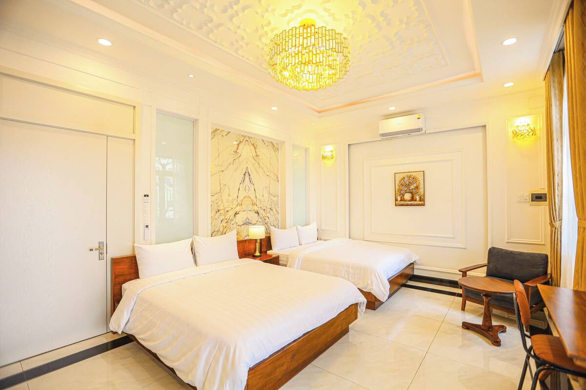A hotel room with two beds, a chandelier, marble wall, and a dining area.