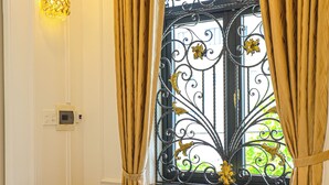 Una habitación con una silla y una pequeña mesa redonda, una ventana con rejas de hierro decorativas y una lámpara fijada a la pared.
