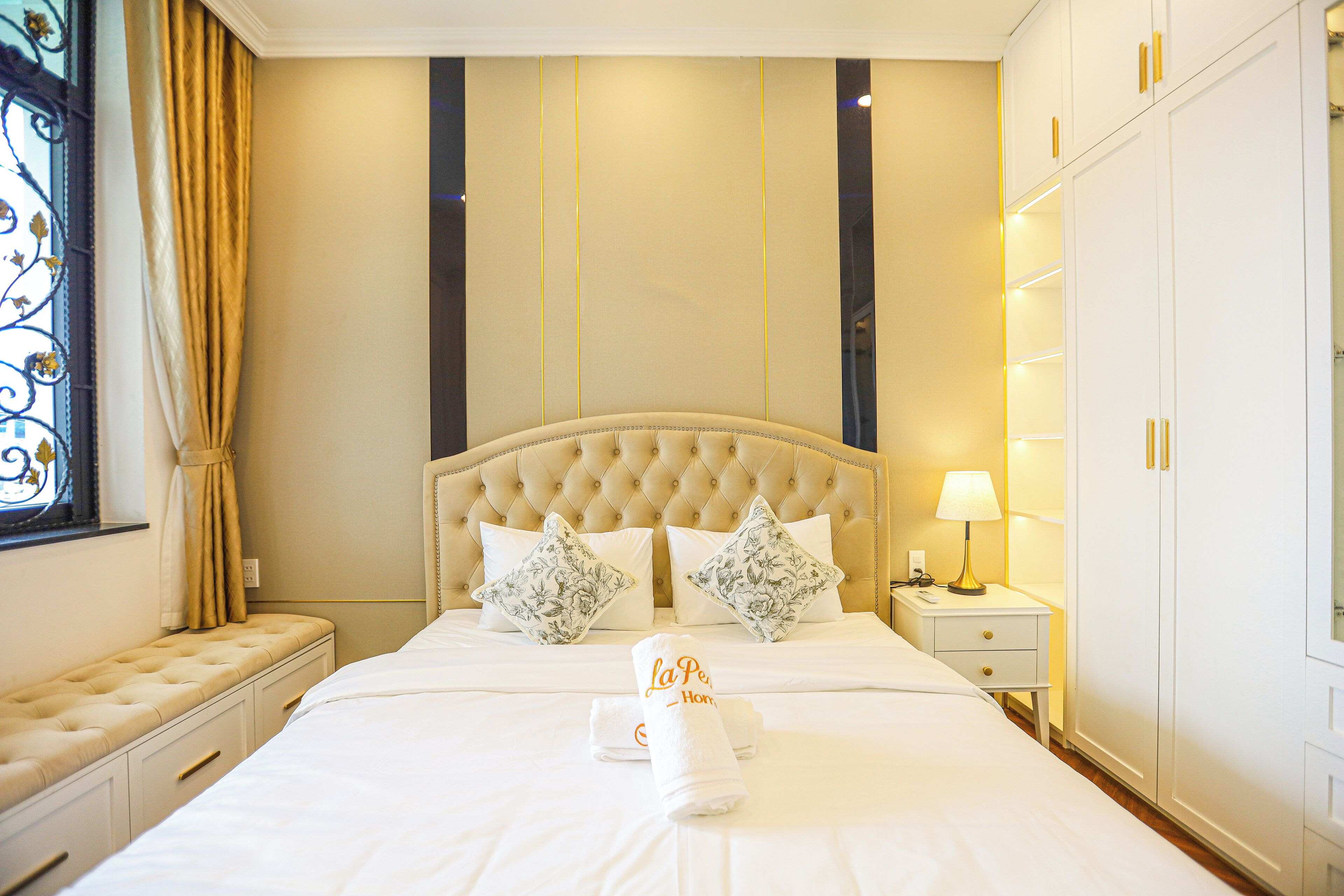 A hotel room with a large bed, two pillows, a bedside table with a lamp, and a wardrobe.