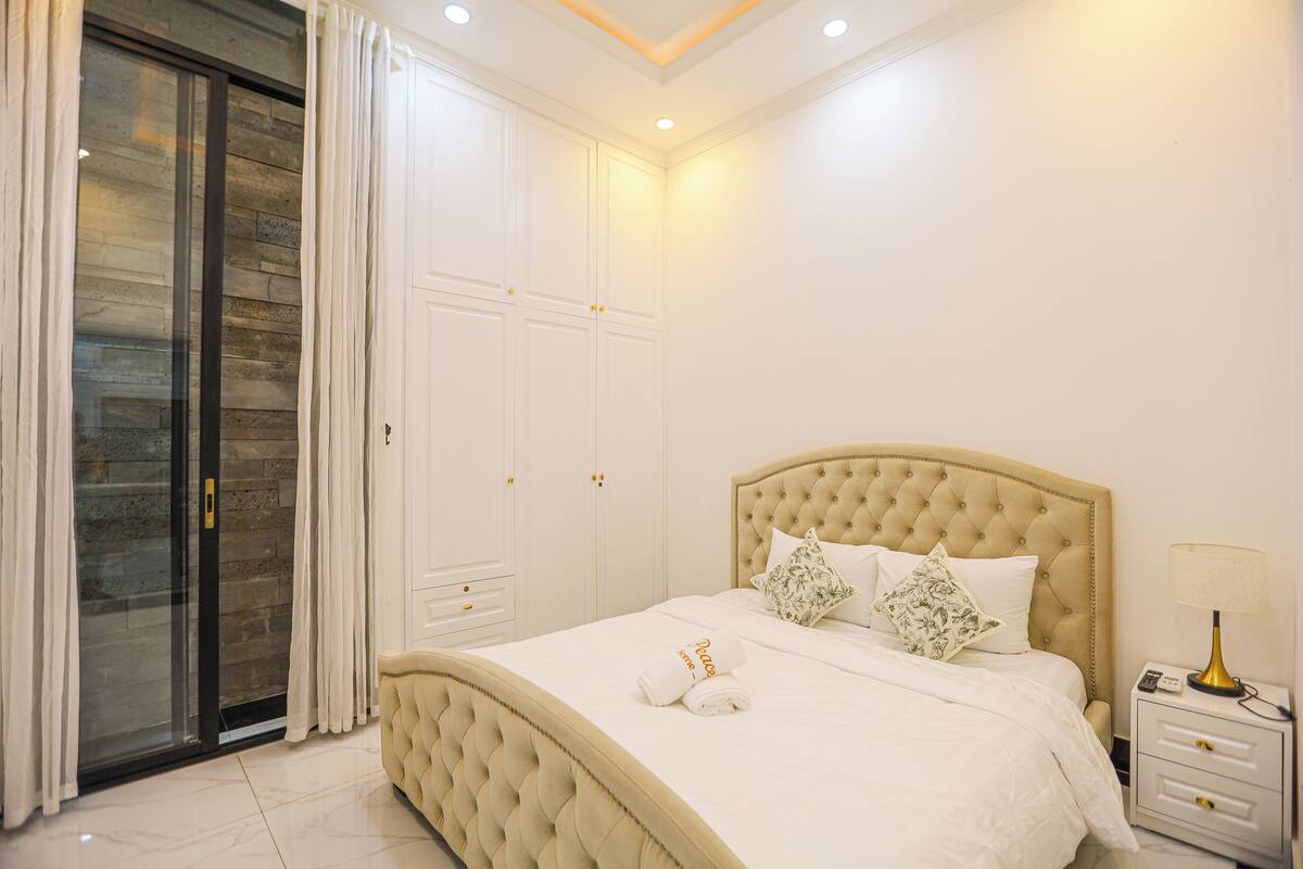 A bedroom with a large bed, a wardrobe, a nightstand, and a sliding glass door.