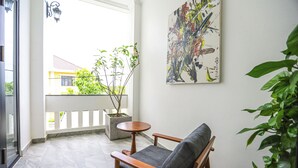 Un balcón con una silla de madera, una planta en maceta y un cuadro en la pared.