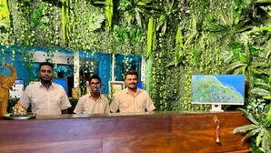 A reception desk with three staff members, surrounded by lush green foliage and a map display. - Sundaras Family Suites (Dambulla)