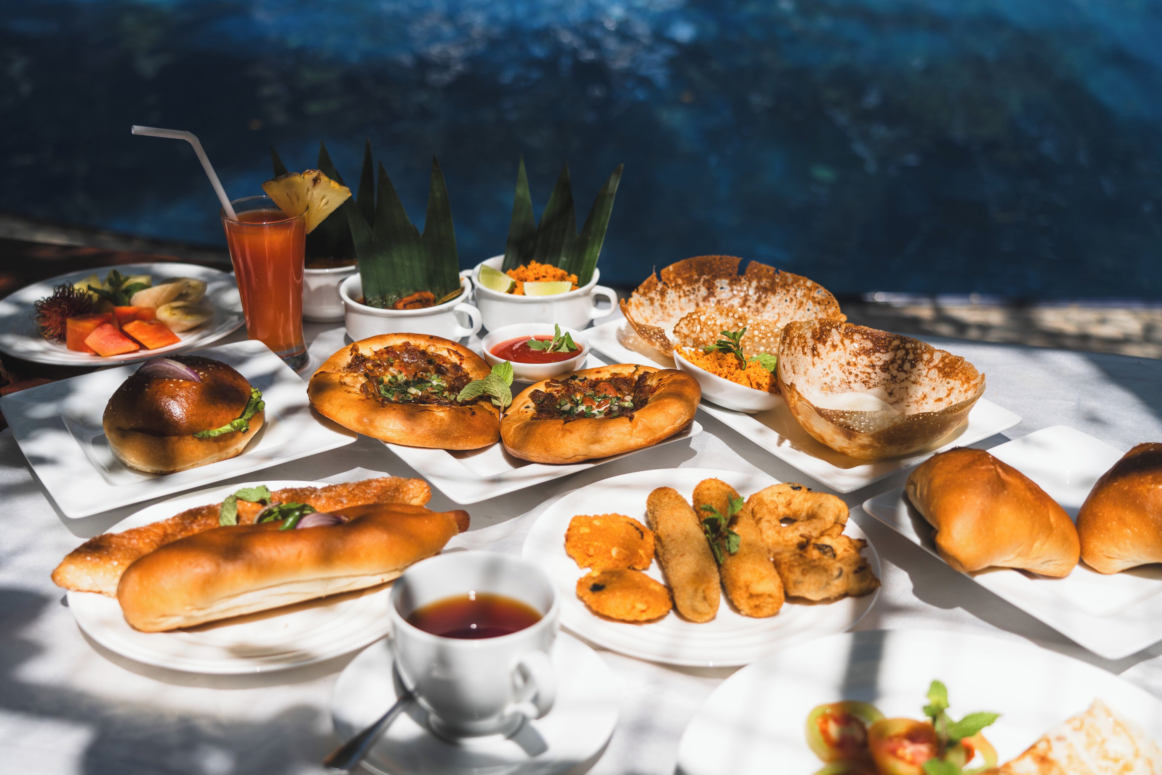Variedad de alimentos, como sándwiches, pasteles y una bebida, dispuesta sobre una mesa, con una piscina al fondo.