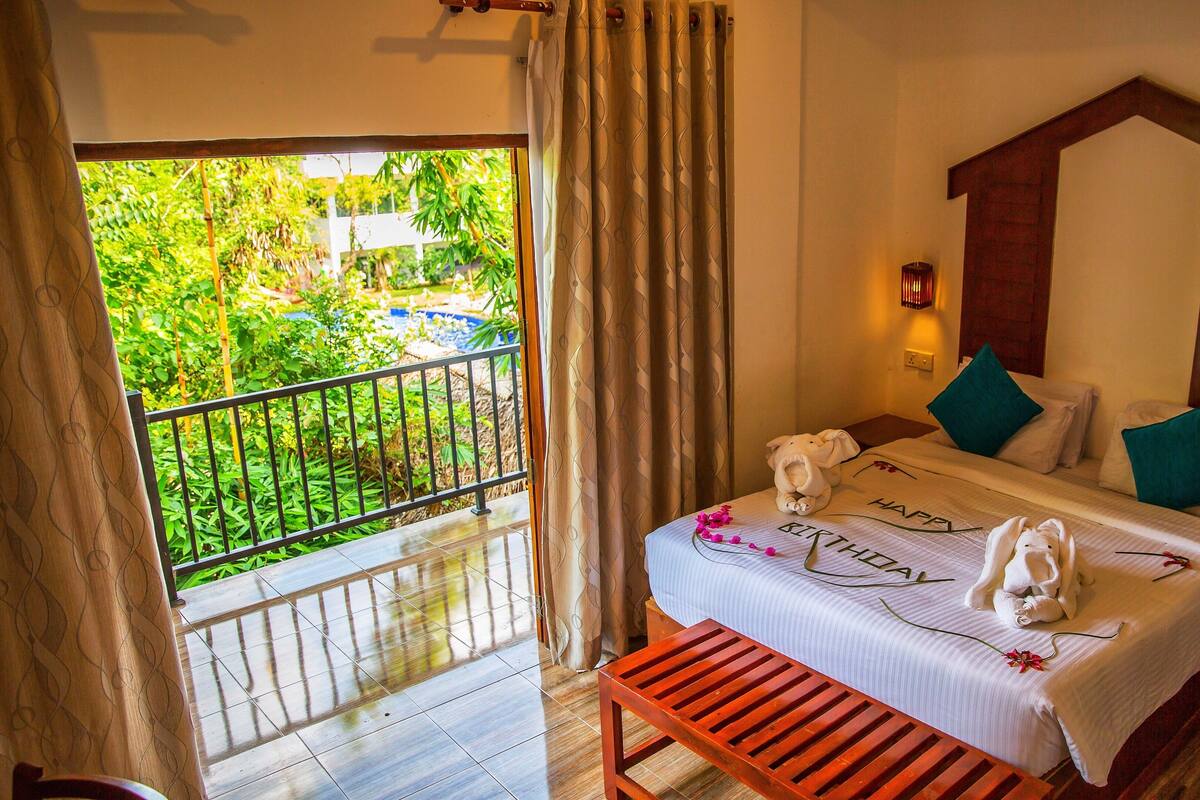 A hotel room with a balcony, a bed with towels, a nightstand, and a phone.