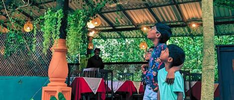 An outdoor restaurant with a covered patio, tables with red and white tablecloths, and hanging lights.