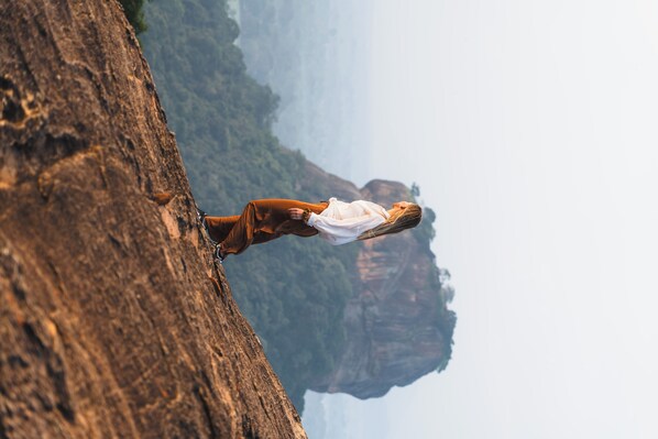 A person standing on a rocky outcrop with a mountainous landscape in the background. - Sundaras Family Suites (Dambulla)
