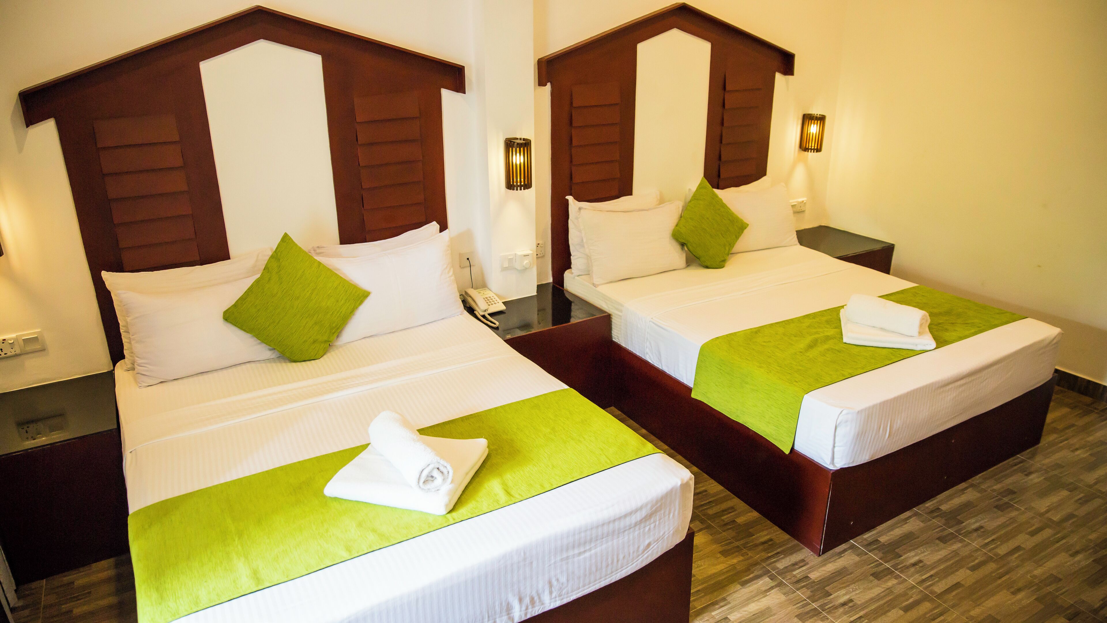 Two identical twin beds with wooden headboards, green bedspreads, and white linens. Each bed has a bedside table with a lamp and a phone.
