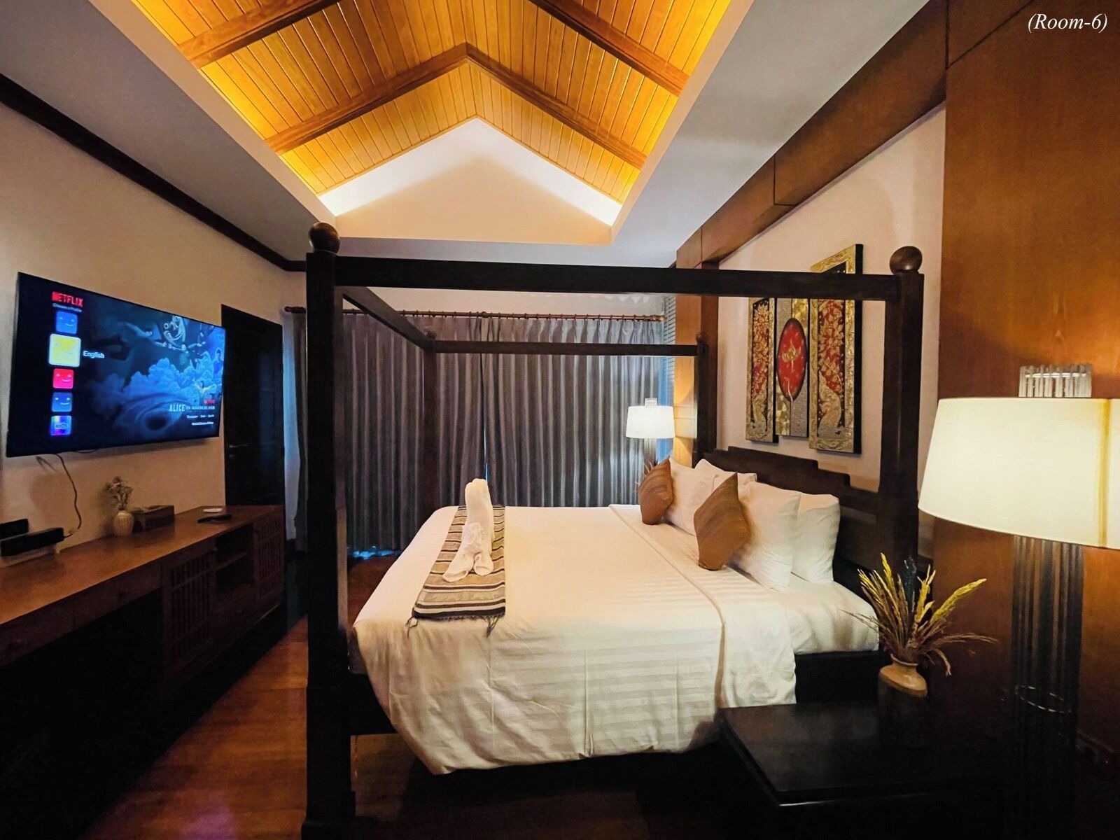 Une chambre d’hôtel dotée d’un lit à baldaquin, d’un téléviseur à écran plat fixé au mur, d’une table de chevet avec une lampe et d’un élément décoratif mural.