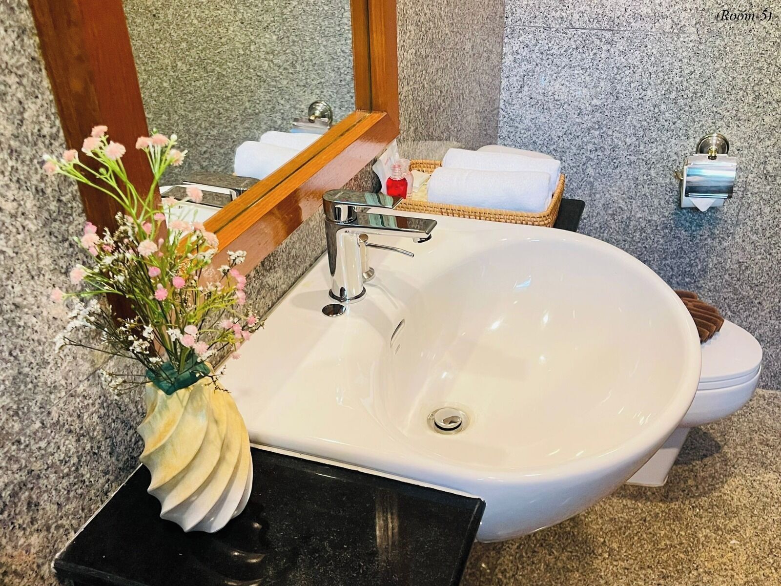 Un baño con lavamanos blanco, espejo, inodoro y una cesta de mimbre con toallas.