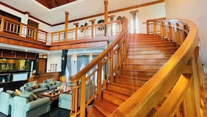 Un hall d’entrée spacieux avec un escalier en bois, un coin salon avec des canapés et une vue sur l’étage supérieur.