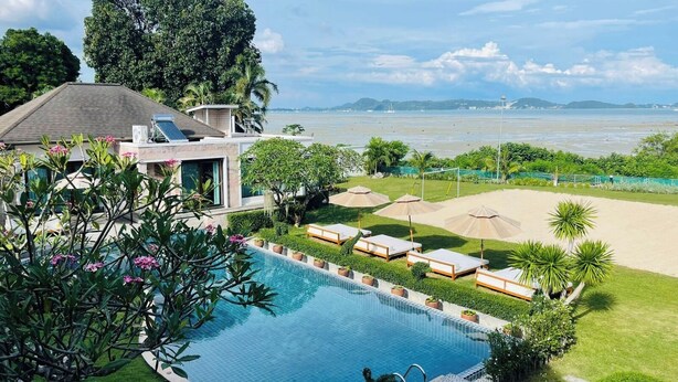 Une piscine entourée de verdure, avec des chaises longues et des parasols, offrant une vue sur la mer.
