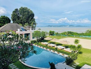 A pool with lounge chairs and umbrellas, surrounded by greenery and a view of the sea. - Kiri Anda Villa Phuket (Rawai)