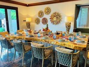 A dining area with a long table set for multiple guests, surrounded by wicker chairs. - Kiri Anda Villa Phuket (Rawai)