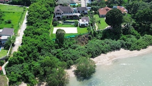 Vue aérienne d’un quartier résidentiel situé sur la côte, avec des maisons, une plage et une végétation luxuriante.