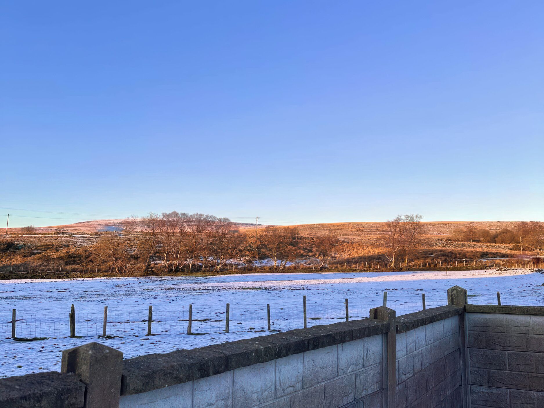 A snow-covered field with a stone wall and a wire fence.