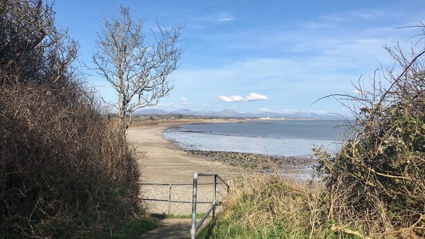 Un sentier côtier qui mène à une plage offrant une vue dégagée sur la mer et les montagnes lointaines.