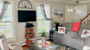 Una sala de estar con un sofá gris, sillones, una mesa de centro, un televisor de pantalla plana y una escalera.