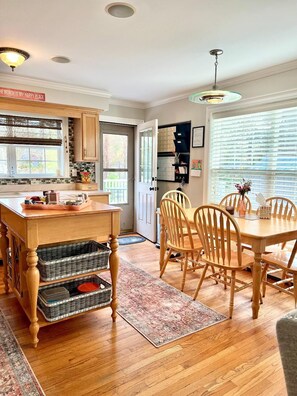Een keuken met houten kastjes, een eettafel met stoelen en een keukeneiland met manden.