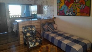 Un salon chaleureux avec un canapé, un fauteuil à motifs floraux, une table basse en bois et un tableau abstrait aux couleurs vives accroché au mur.