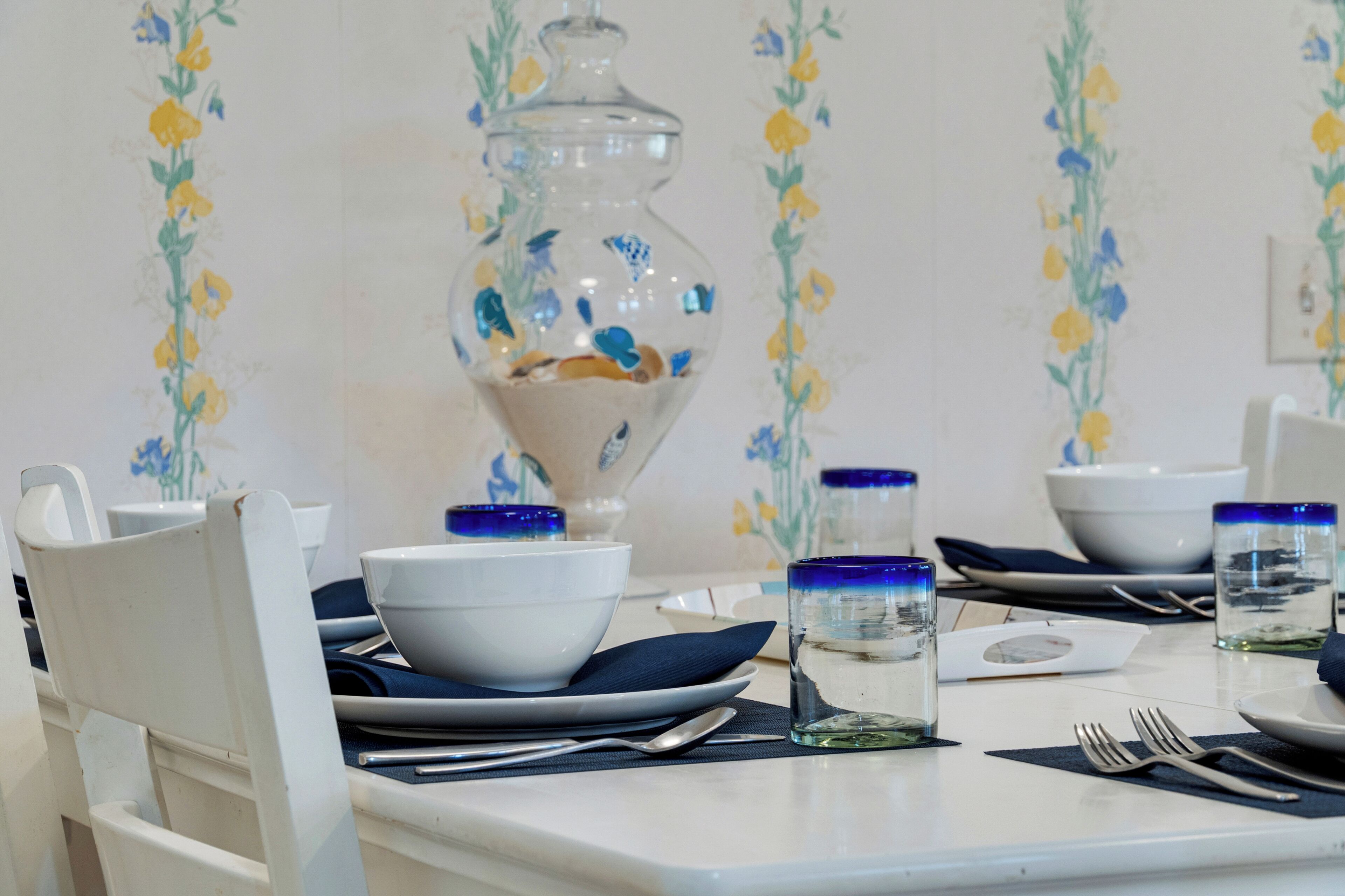 A dining table set with white plates, blue napkins, and clear glass water glasses.