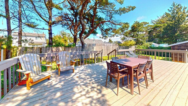 Eine Holzterrasse mit Tisch und Stühlen, umgeben von einem Holenzaun und Bäumen.
