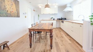 A modern kitchen with white cabinets, a wooden dining table, and a large painting on the wall.