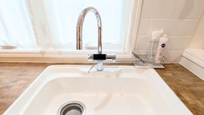 A white kitchen sink with a modern faucet, a stainless steel drain, and a wooden floor.