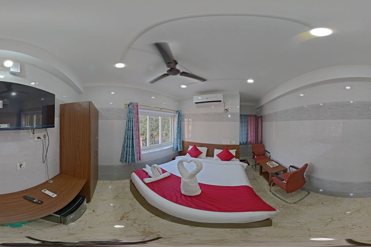 A modern hotel room with a curved bed, a ceiling fan, a TV, and a wooden wardrobe.