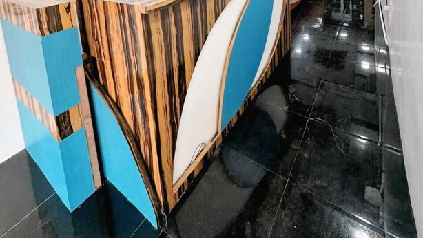 Un espace d’accueil doté d’un comptoir de réception en bois aux lignes courbes, d’un sol carrelé de couleur noire et d’un design de plafond moderne.