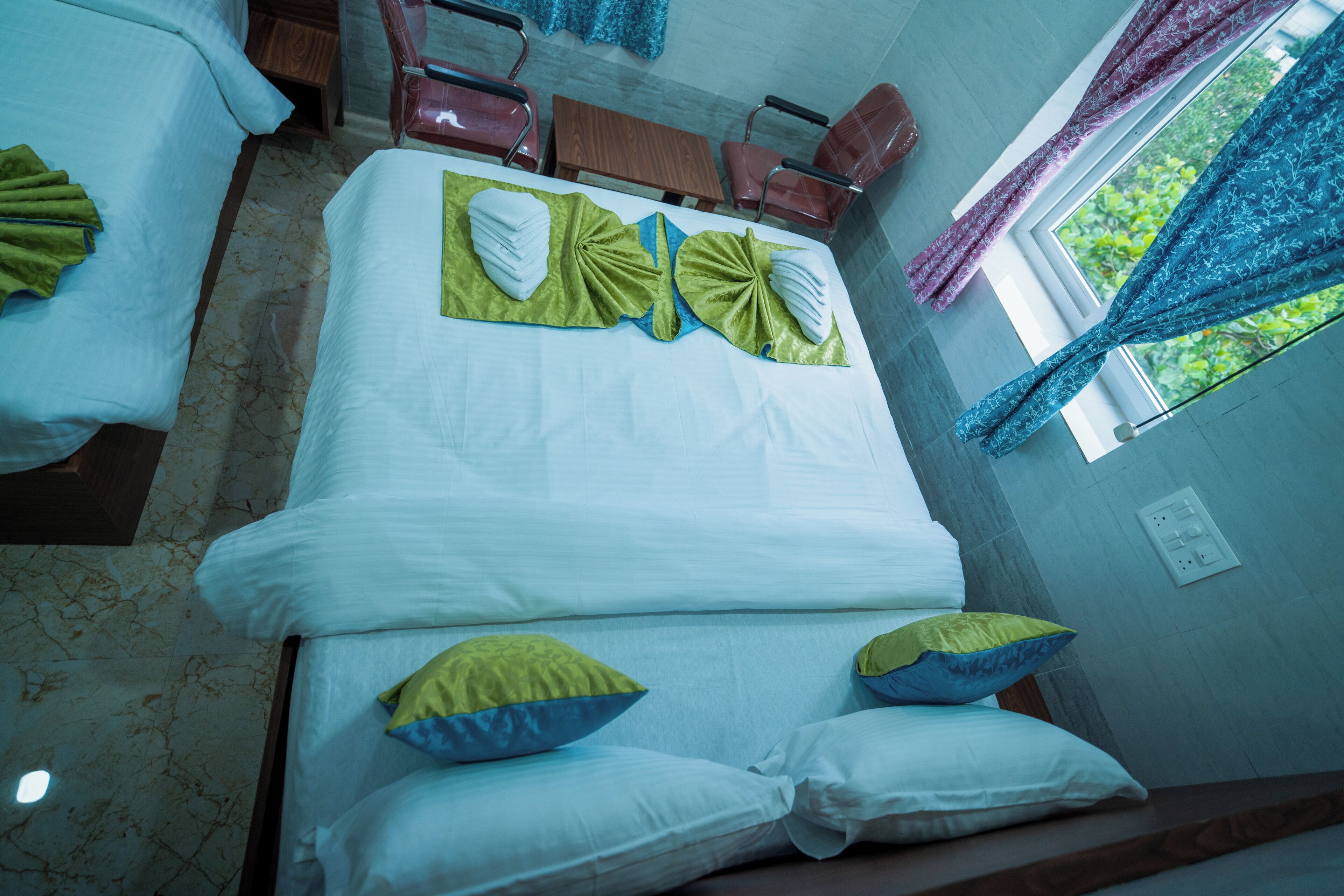 Een hotelkamer met een groot bed, twee stoelen, een tafeltje en een raam met gordijnen.
