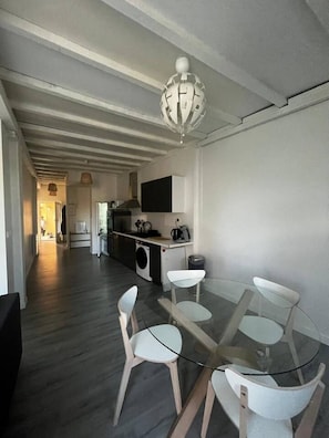 Une cuisine moderne avec un coin repas comprenant une table en verre et des chaises blanches.