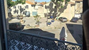 Un balcon orné d’une balustrade en fer forgé, une vue sur une rue résidentielle bordée de voitures garées et des immeubles à l’architecture traditionnelle.