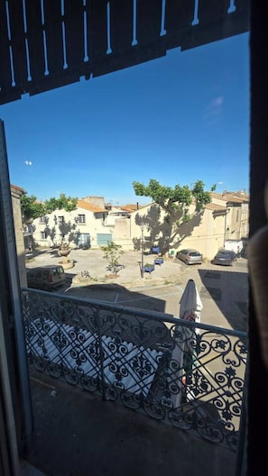 Un balcon orné d’une balustrade en fer forgé, une vue sur une rue résidentielle bordée de voitures garées et des immeubles à l’architecture traditionnelle.