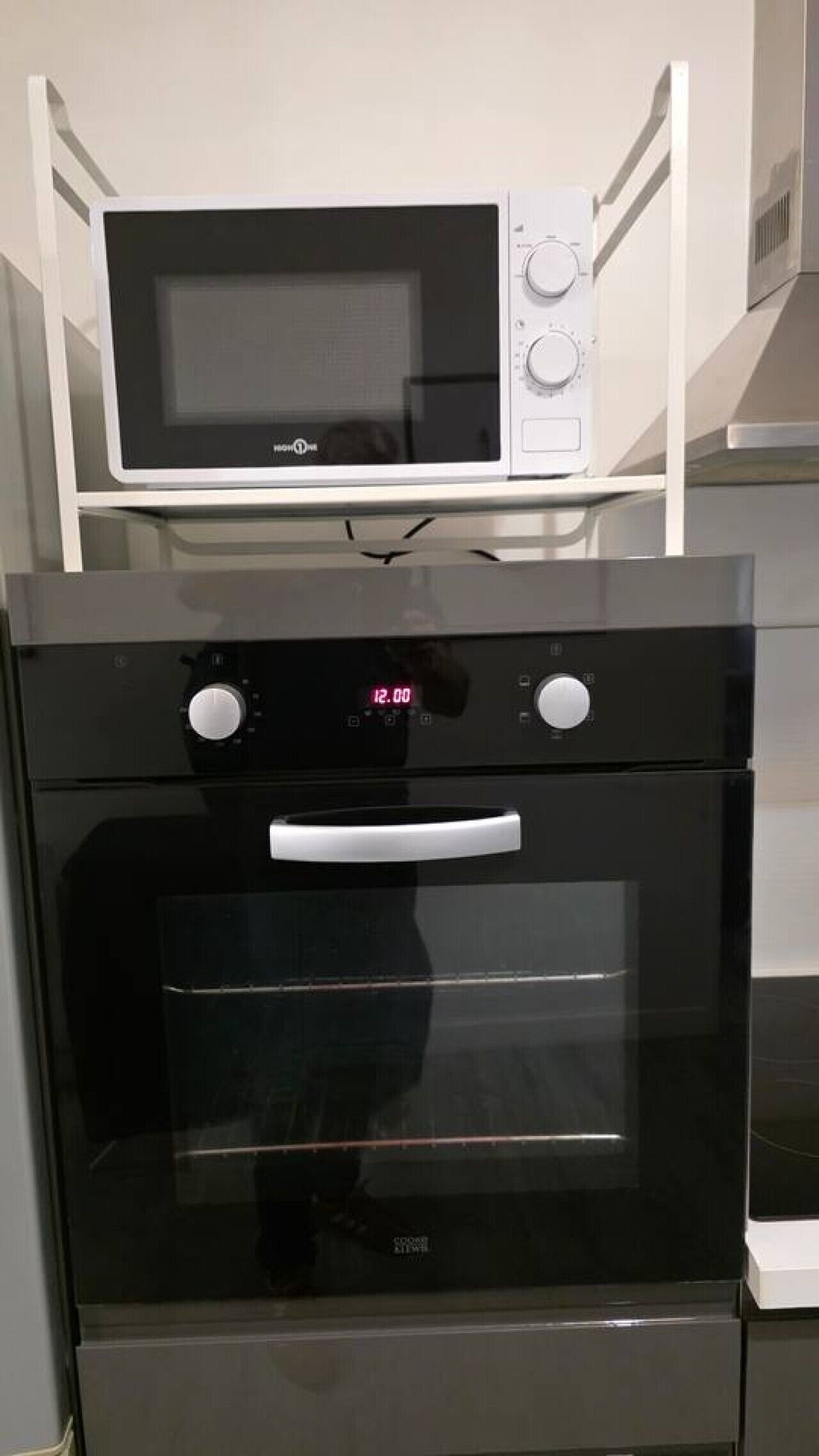 A kitchen with a microwave on top of a stove, a digital clock, and a control panel.