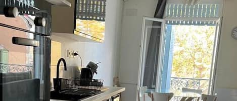 A modern kitchen with stainless steel appliances, a dining area with wooden chairs, and a large window with a view.