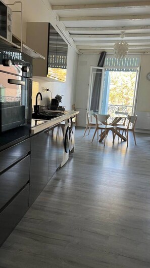 Een moderne keuken met roestvrijstalen apparatuur, een eetgedeelte met houten stoelen en een groot raam met uitzicht.