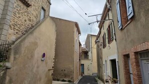 Une rue étroite, bordée de bâtiments des deux côtés, avec un beffroi et une place de stationnement signalée par un symbole de cygne.