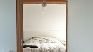 Ein Schlafzimmer mit Holzboden, einem Bett mit weißer Bettwäsche, einem grauen Teppich und einer Pendelleuchte.