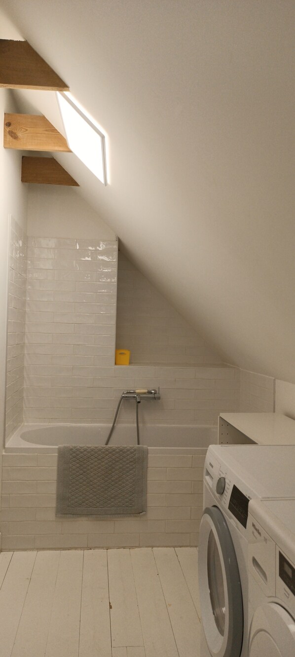 A laundry room with a washing machine, a towel rack, and a bathtub.