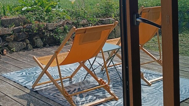 Eine Holzterrasse mit Gartenmöbeln, Blick zum Himmel und eine Steinmauer.