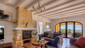 A living room with a stone fireplace, a television, a sofa, and a view of the outdoors.