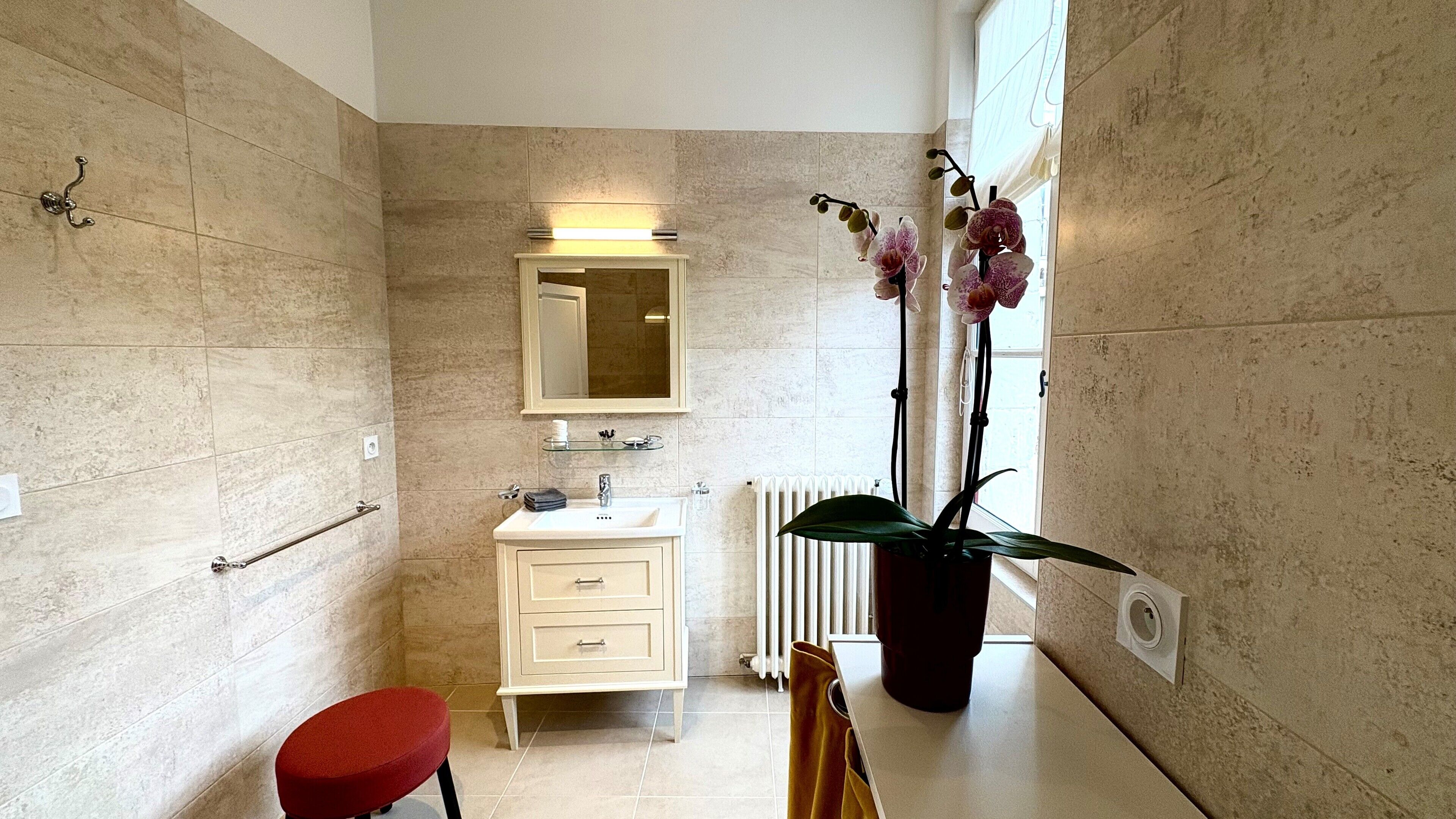 Une salle de bain moderne avec un meuble-lavabo blanc, un miroir, un radiateur et une plante orchidée en pot.