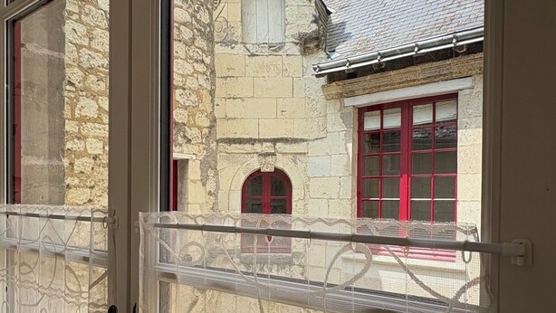 Una ventana con vistas a un edificio de piedra con ventanas rojas y techo de tejas.