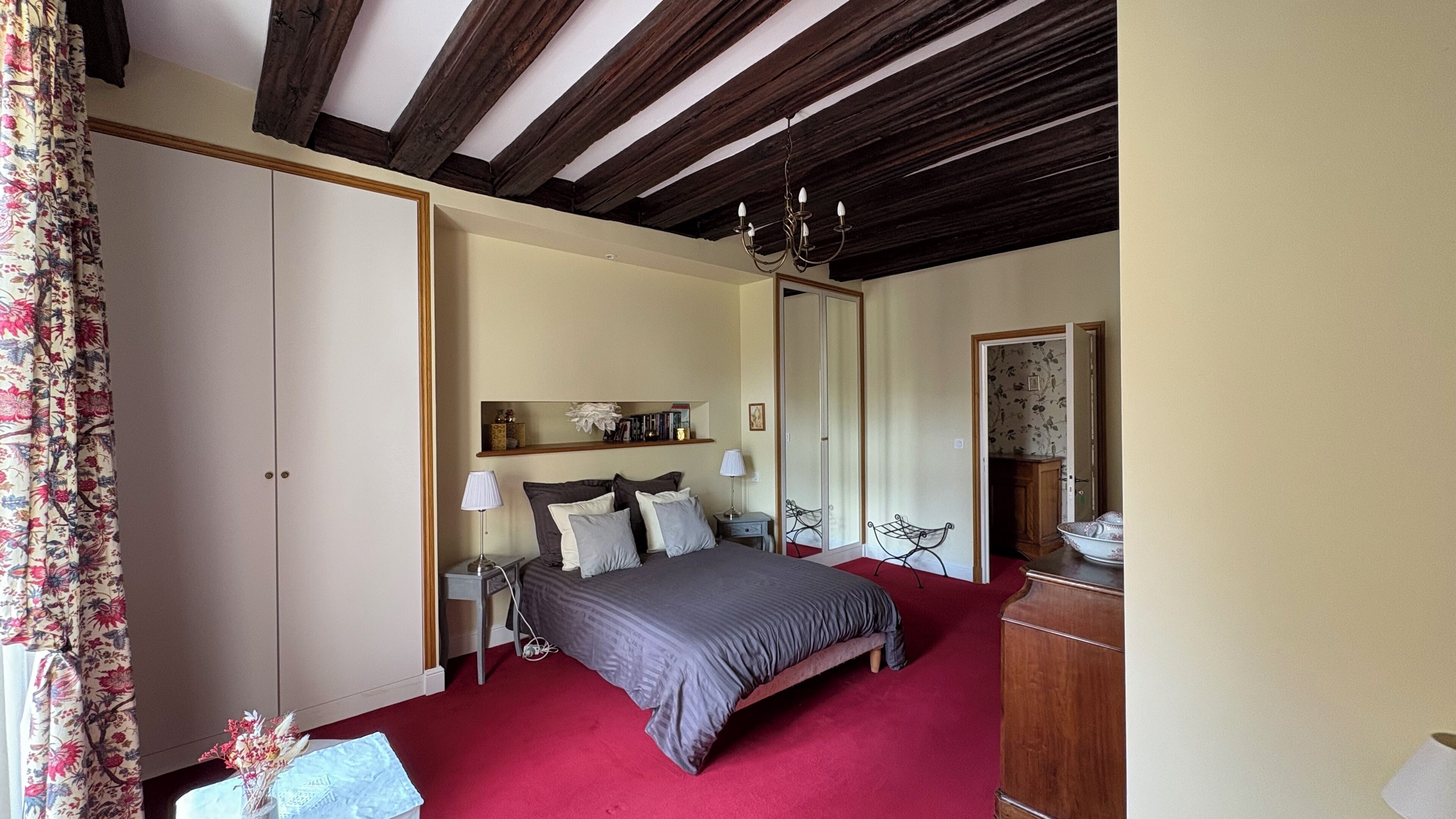 A bedroom with a bed, bedside tables, a mirror, a wardrobe, and a red carpet.